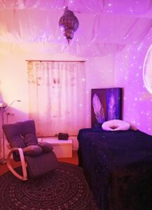 Ein Rückzugsort für Mutter und Kind. Der in sanften, warmen Farben beleuchtete Raum hat eine mit Stoff abgehängte Decke, einen Schaukelstuhl und eine Liege. Ein Sternenhimmel ist in die Umgebung projeziert.